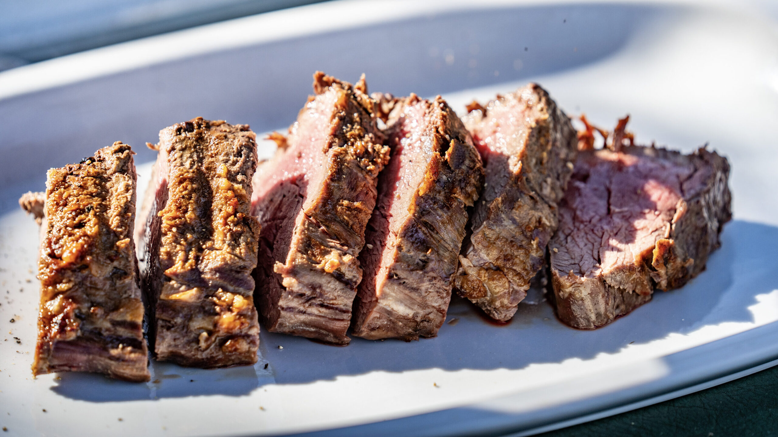 Slices of grilled beef arranged on a white serving plate, showing a tender, cooked interior