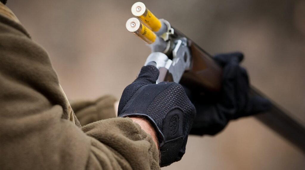 Gloved hands load two yellow shells into an over-and-under shotgun