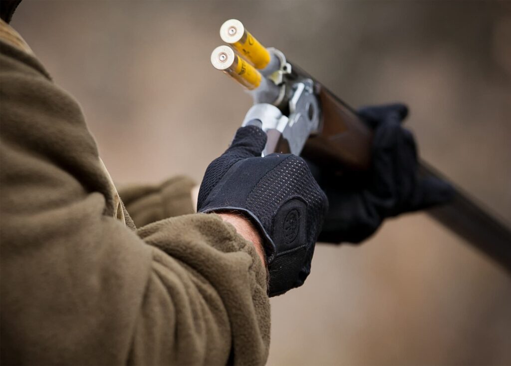 Gloved hands load two yellow shells into an over-and-under shotgun